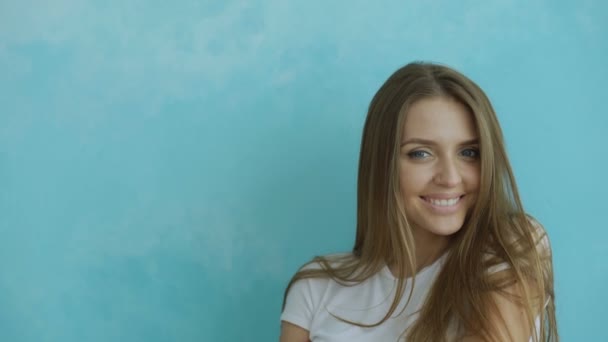 Vértes portré fiatal mosolyogva és nevetve nő keresi a kamera a kék háttér — Stock videók