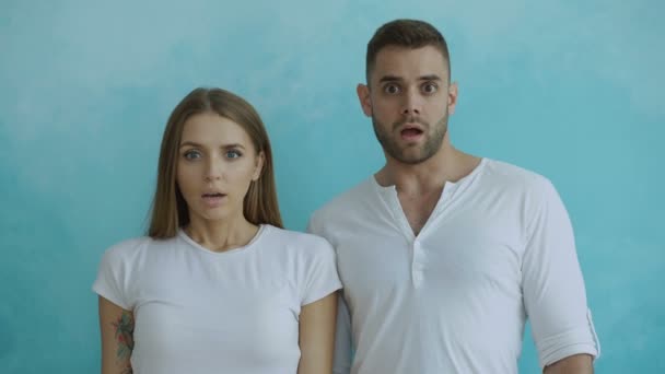 Portrait of young couple actively surprising and wondering looking into camera on blue background — Stock Video