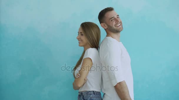 Jovem casal de pé de volta para trás flertando uns aos outros e virar para o beijo no fundo azul — Vídeo de Stock