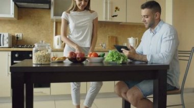 Kadar erken sabah mutfakta sohbet çekici çift eğimli. Yakışıklı adam kız arkadaşı yemek yaparken tablet kullanma
