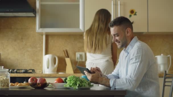 Casal atraente conversando na cozinha de manhã cedo. Mulher bonita alimentar seu marido enquanto cozinha café da manhã — Vídeo de Stock