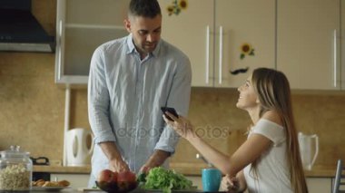 Sabah mutfakta çekici çift. Güzel kız erkek arkadaşı ile smartphone cep telefonu ile sosyal medya paylaşımı