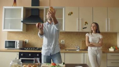 Çekici sevgi dolu çift mutfakta eğleniyor. Yakışıklı bir adam kız arkadaşını etkilemek için elma ile hokkabazlık