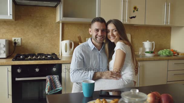 Retrato de feliz pareja sonriente sentada en la cocina temprano en la mañana en casa — Vídeos de Stock