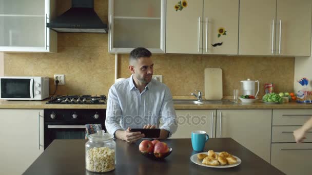 Attraktives junges Paar, das sich frühmorgens in der Küche umarmt und küsst, während der Mann frühstückt — Stockvideo