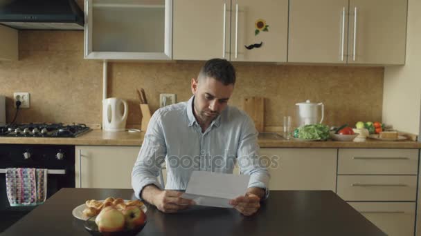 Joven indeciso leyendo facturas impagadas y abrazado por su esposa apoyándolo en la cocina en casa — Vídeos de Stock