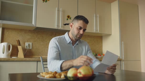 Joven indeciso leyendo facturas impagadas y abrazado por su esposa apoyándolo en la cocina en casa — Vídeo de stock