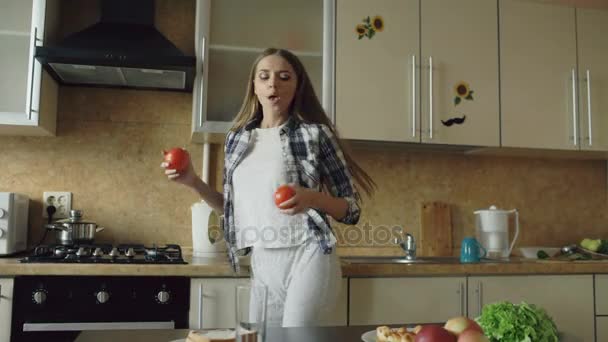 Fröhliche junge lustige Frau tanzt und singt, während sie frühmorgens in der Küche frühstückt — Stockvideo