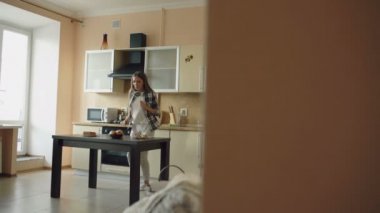 Dans ve kepçe ile evde mutfakta yemek yaparken yaparken şarkı neşeli genç komik kadın