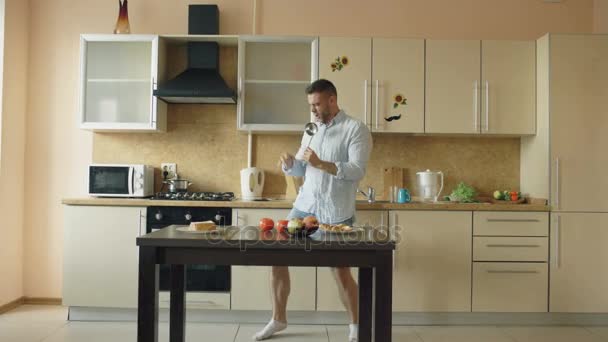 Attraktive junge lustige Mann tanzen und singen mit Schöpfkelle, während das Kochen in der Küche zu Hause — Stockvideo