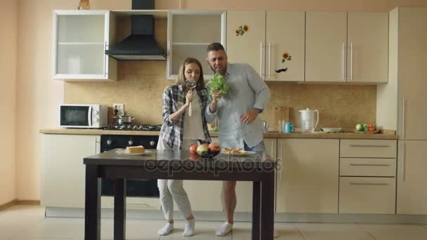 Attraktive junge fröhliche Paare haben Spaß beim Tanzen und Singen, während sie zu Hause in der Küche kochen — Stockvideo