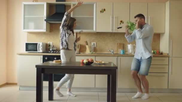 Attraktive junge fröhliche Paare haben Spaß beim Tanzen und Singen, während sie zu Hause in der Küche kochen — Stockvideo