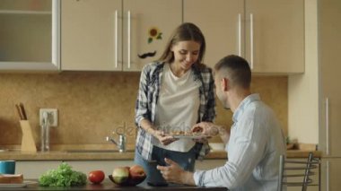 Çekici çift mutfakta. Erkek arkadaşı onu besleme sırasında sörf tablet bilgisayar oynamak