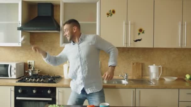 Hombre guapo divirtiéndose en la esgrima de la cocina con cuchara y cuchara mientras cocina el desayuno en casa — Vídeos de Stock