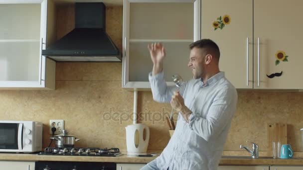 Lento movimiento de atractivo joven divertido bailando y cantando con cucharón mientras se cocina en la cocina en casa — Vídeo de stock