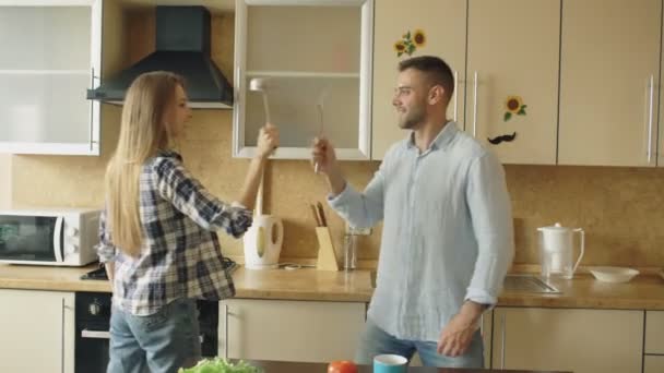 Attraente coppia divertirsi in cucina recinzione con mestolo e cucchiaio mentre si cucina la colazione a casa — Video Stock