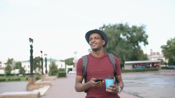 Steadicam disparo de sonriente hombre turístico caminando y surf teléfono inteligente cerca de famoso lugar histórico en Europa — Vídeos de Stock