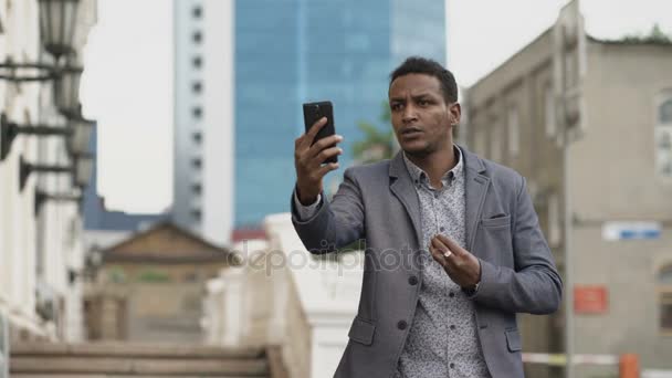 Raza mixta enojado hombre de negocios que tiene chat de vídeo en línea en la conferencia de negocios utilizando el teléfono inteligente — Vídeo de stock