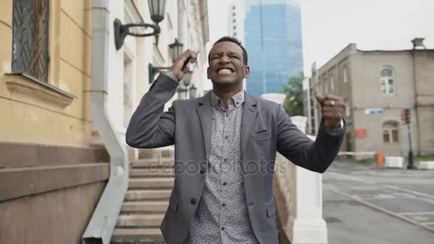 Steadicam shot of Mixte race homme d'affaires joyeux danser et parler téléphone de sa nouvelle carrière — Video