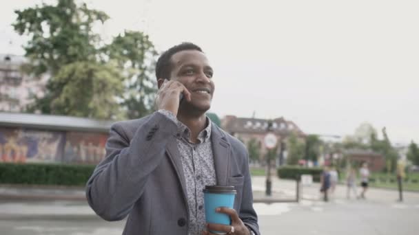 Змішана гонка щасливий бізнесмен розмовляє телефоном і стоїть з чашкою кави на відкритому повітрі — стокове відео