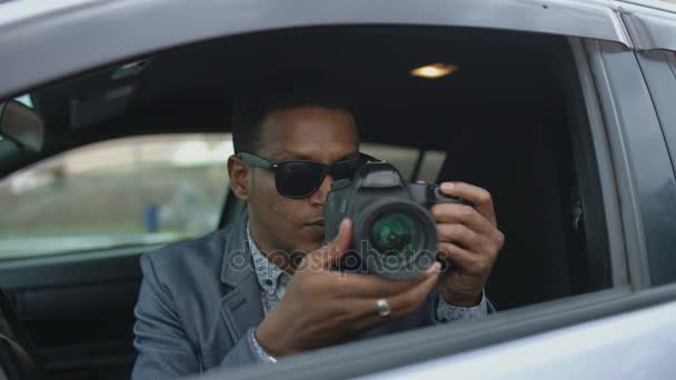 Paparazzi hombre sentado dentro del coche y fotografiando con la cámara dslr — Vídeos de Stock