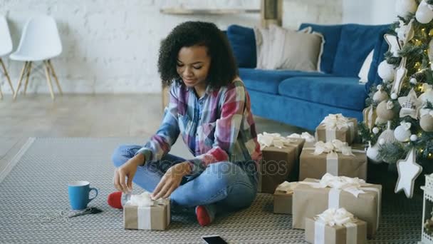 Attraktiva blandad ras tjej packning presentbox nära julgran hemma — Stockvideo