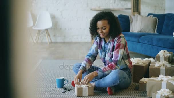Pan shot of Atractiva caja de regalo de embalaje de chica de raza mixta cerca del árbol de Navidad en casa — Vídeos de Stock
