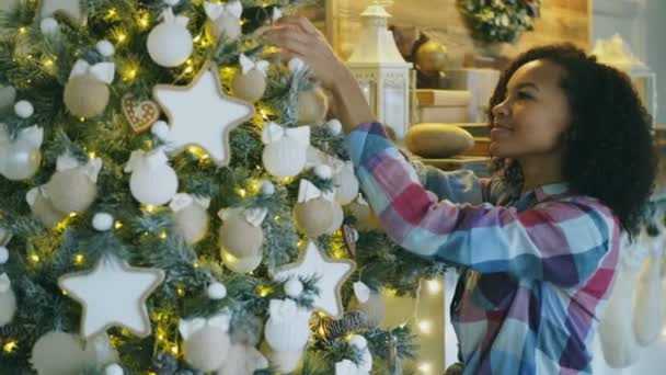 Jolie jeune femme africaine décorant arbre de Noël à la maison se préparant pour la célébration de Noël — Video