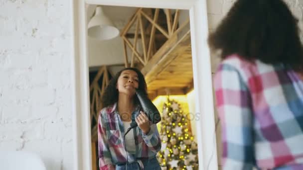 Rizado divertido africano americano chica bailando y cantando con secador de pelo delante de espejo en casa — Vídeos de Stock