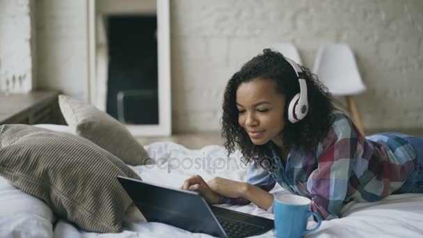Mladá kudrnaté africká americká žena těší poslouchat hudbu na notebooku, když ležel na posteli — Stock video