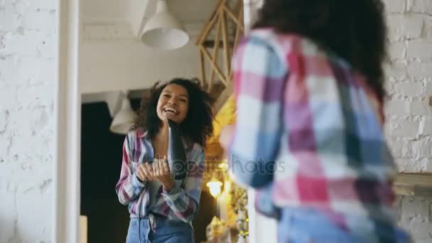 Rizado divertido africano americano chica bailando y cantando con secador de pelo delante de espejo en casa — Vídeos de Stock