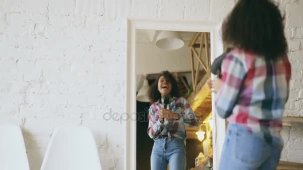 Göndör vicces afro-amerikai lány táncol és énekel, hajszárítóval felszerelt, otthon a tükör előtt — Stock videók