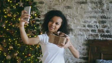 Kıvırcık genç kız evde Noel ağacı yakınındaki Smartphone kamera kullanarak online sohbet sohbet