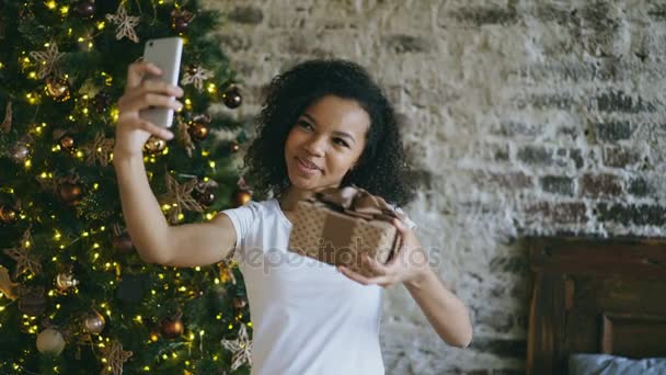 Adolescente rizado chateando conversación en línea utilizando la cámara del teléfono inteligente en casa cerca del árbol de Navidad — Vídeos de Stock