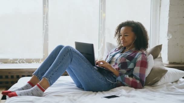 Menina de raça mista feliz ter vídeo chat com amigos usando câmera laptop enquanto deitado na cama — Vídeo de Stock