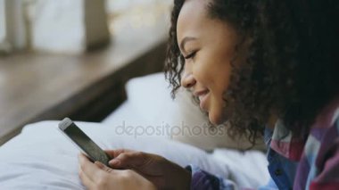 Afrikalı kız evde yatakta yatıyordu süre smartphone cep telefonu ile online fotoğraf izlerken Close-Up