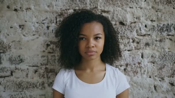Retrato de encaracolado Africano americano adolescente menina ativamente surpreendente e querendo saber sobre tijolo parede fundo — Vídeo de Stock