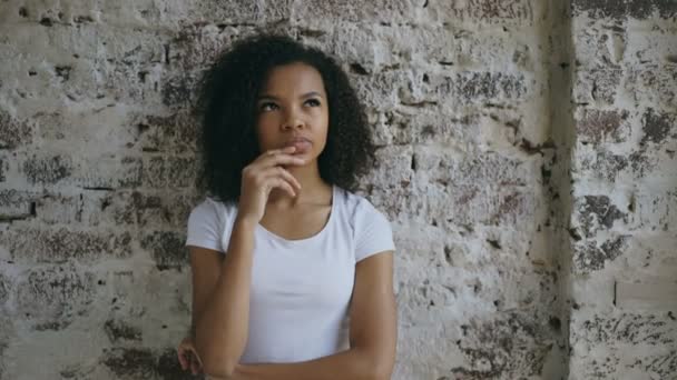 Pensativo jovem mista menina pensando em resolver o problema no fundo da parede de tijolo — Vídeo de Stock