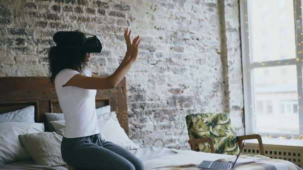Curly menina adolescente de raça mista recebendo experiência usando óculos VR 360 de realidade virtual em casa — Vídeo de Stock
