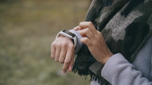 Zbliżenie przechylić się strzał mieszanej rasy student dziewczyna za pomocą zegarka smartwatch i uśmiechając się w pobliżu univercity — Wideo stockowe