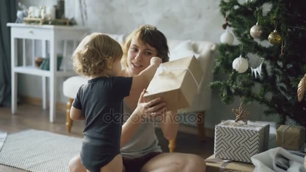 Lycklig mamma och hennes lilla dotter packa upp presentbox nära granen hemma — Stockvideo