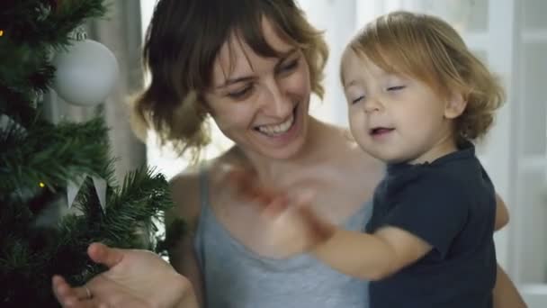 Счастливая мать и ее маленькая дочь играют у елки дома — стоковое видео