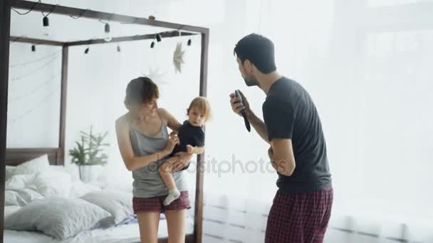 Famille heureuse et petite fille mignonne dansant près du lit dans la chambre à coucher tout en chantant célèbre à la maison — Video