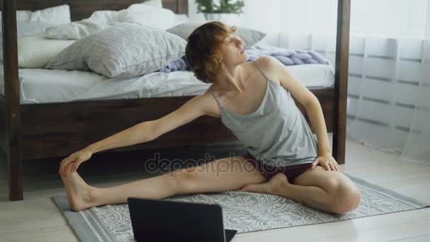Mujer atractiva joven haciendo ejercicio de yoga y viendo lección de tutorial en el ordenador portátil en casa — Vídeos de Stock