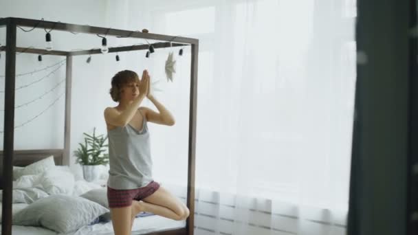 Joven hermosa mujer haciendo ejercicio de yoga cerca de la cama en el dormitorio en casa — Vídeos de Stock