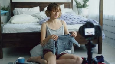 Evde dslr fotoğraf makinesi ile video blog çocuk moda hakkında kayıt yatak yakınında oturan çekici neşeli kadın