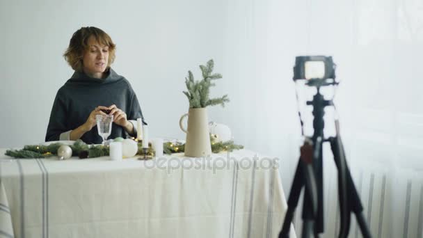 Привлекательная веселая женщина, сидящая за столом и записывающая видео блог о дизайне сервировки стола на камеру — стоковое видео