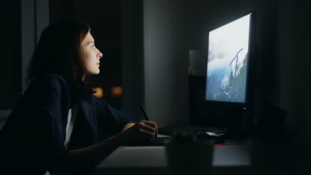 Concentrated young woman designer working in office at night using computer and graphics tablet to finish job — Stock Video