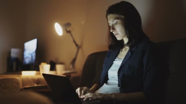 Mujer joven concentrada que trabaja por la noche usando ordenador portátil y escribiendo mensaje — Vídeo de stock