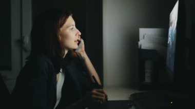 Konsantre kadın tasarımcı konuşurken telefon çalışma ofisinde gece işi bitirmek için bilgisayar ve grafik tableti kullanarak